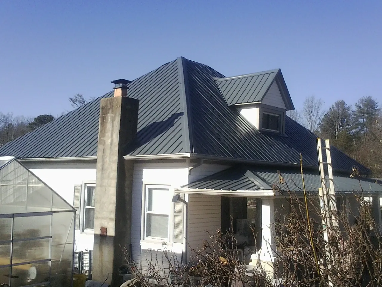 Dark blue standing seam metal roof on a white farmhouse with dormer — Slate & Tile Roof Repair by Roofing Brothers in Penney Farms
