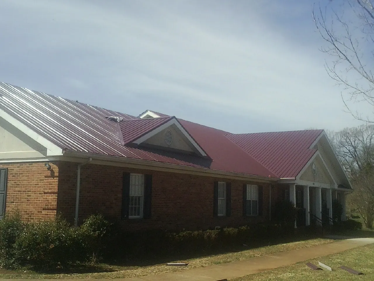 Red metal roof with gabled entries on a long brick building, from a Hail Damage Roof Repair job in Penney Farms