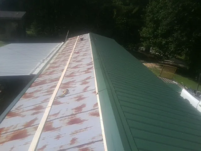 Old rusted panels beside newly installed green metal roofing — Wind Damage Roof Repair by Roofing Brothers in Penney Farms