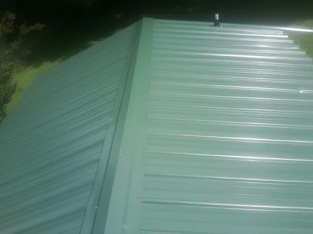 New green metal panels meeting at the ridge of a roof — Flat Roof Repair work by our crew in Penney Farms