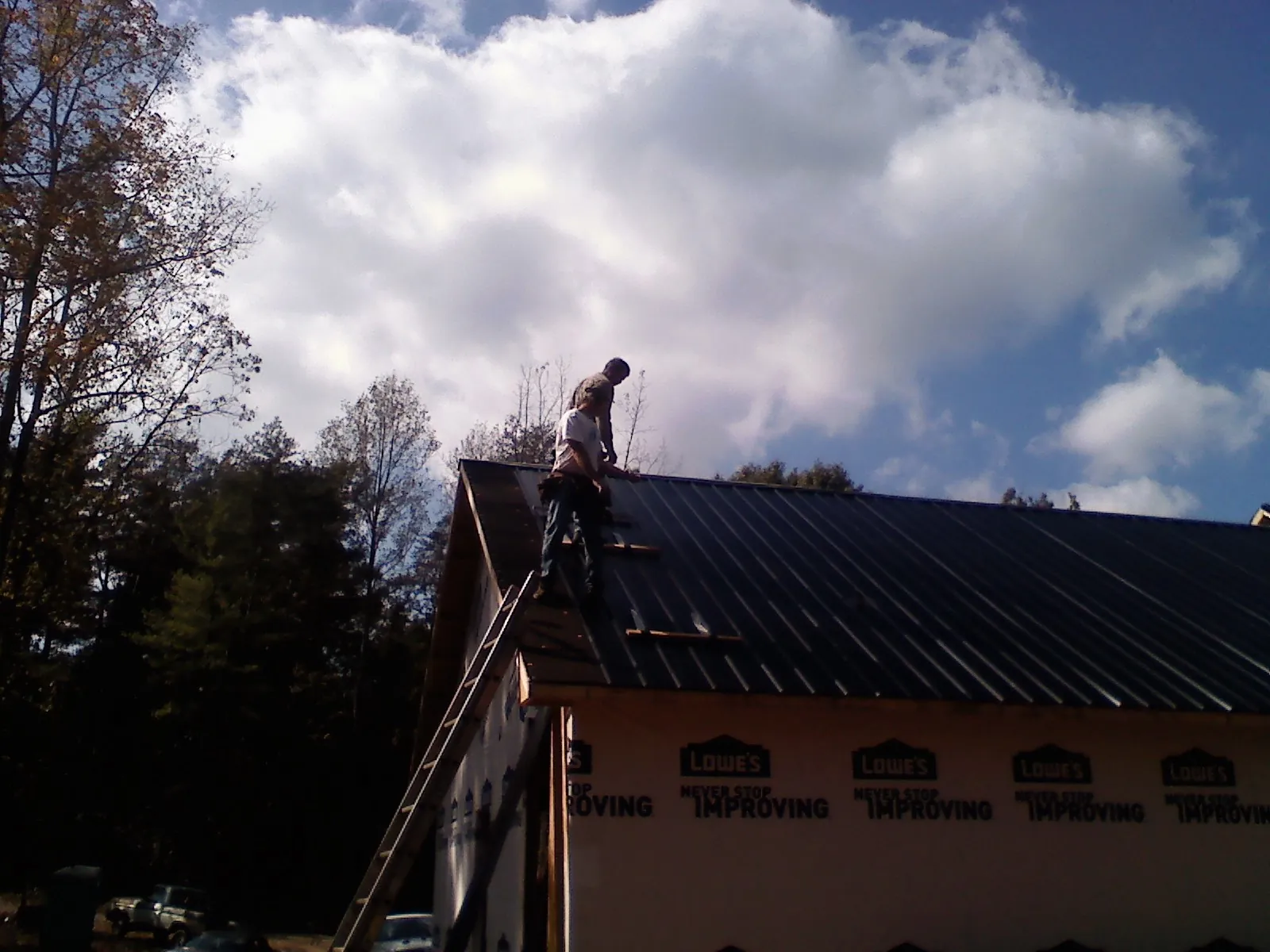 Roofer fastening dark metal panels high against a cloudy sky, from a Roof Inspection job in Penney Farms