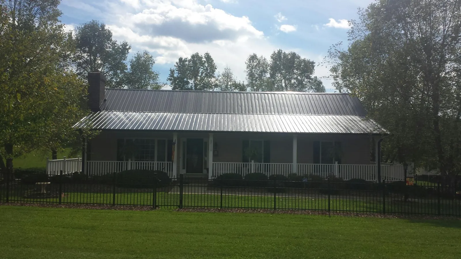 Gray metal roof on a brick ranch with a full width front porch — Gutter Guard Installation work by our crew in Penney Farms