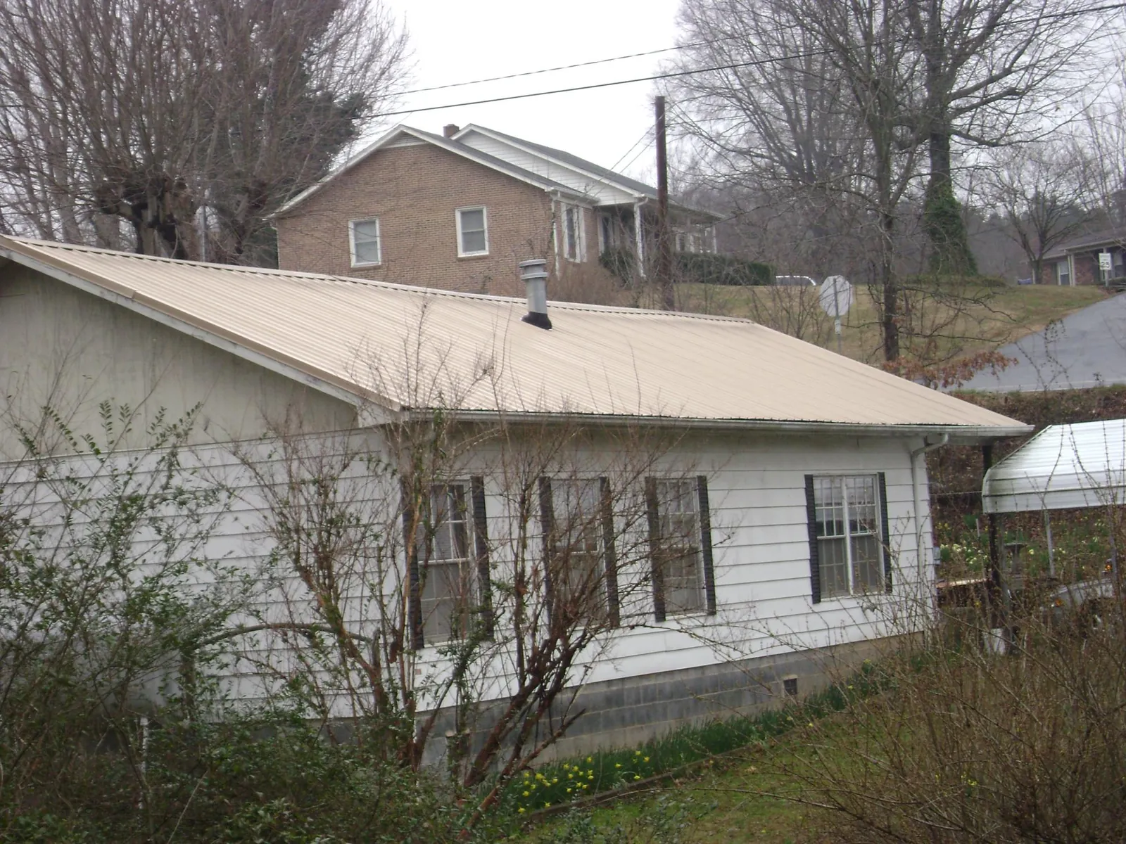Tan metal roof on a white sided house set into a hillside — Commercial Roofing by Roofing Brothers in Penney Farms