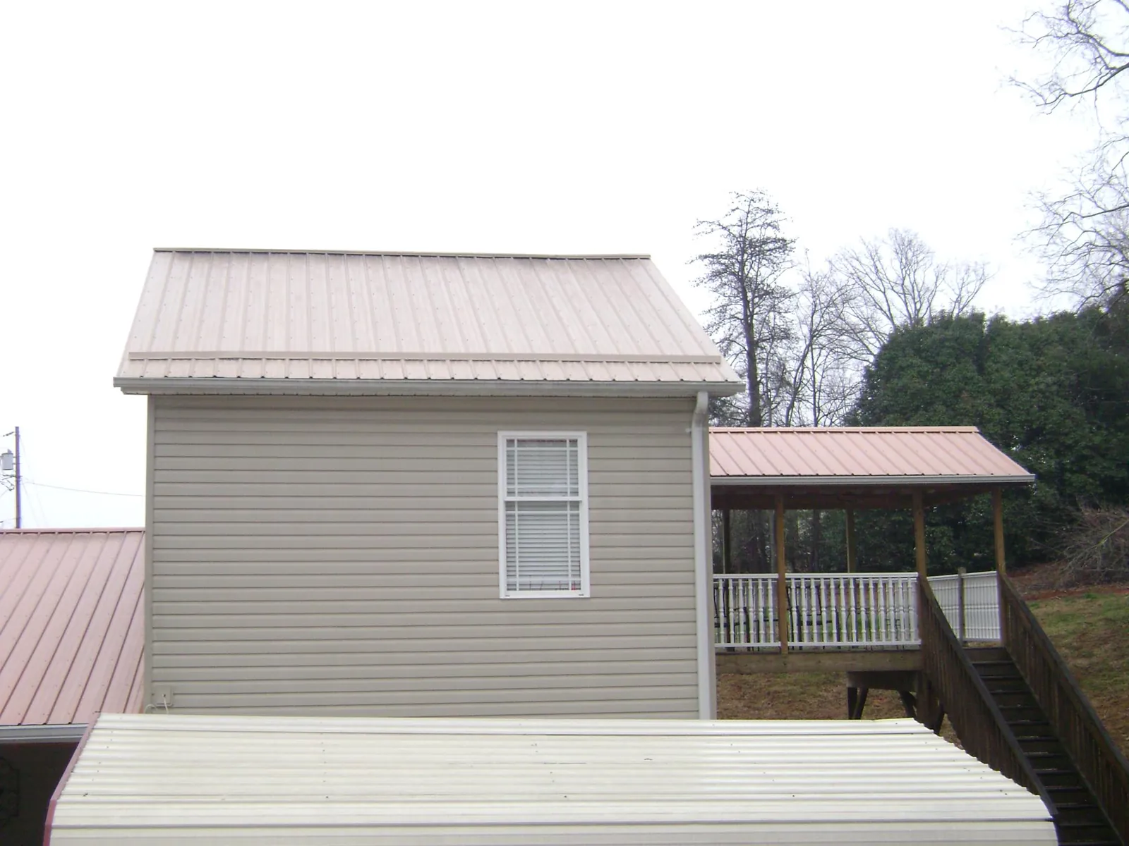 Tan metal roofs on a two story addition and attached porch, from a Roof Replacement job in Penney Farms